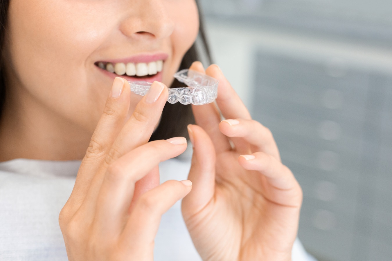 Woman placing a clear aligner tray over her upper teeth