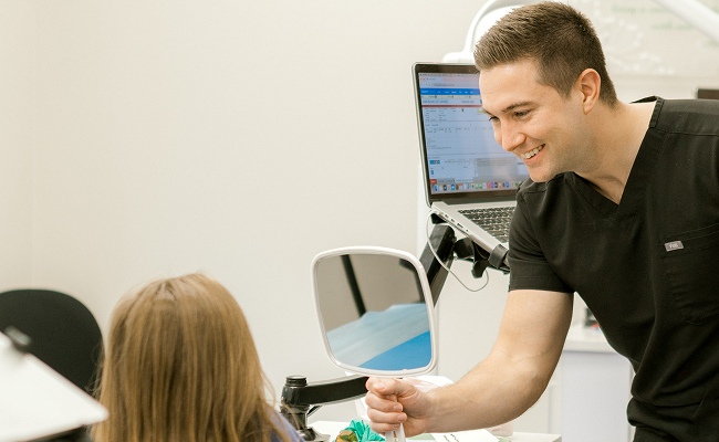 Dr. Jared Teeples showing a smiling teen her treatment images on a chairside laptop