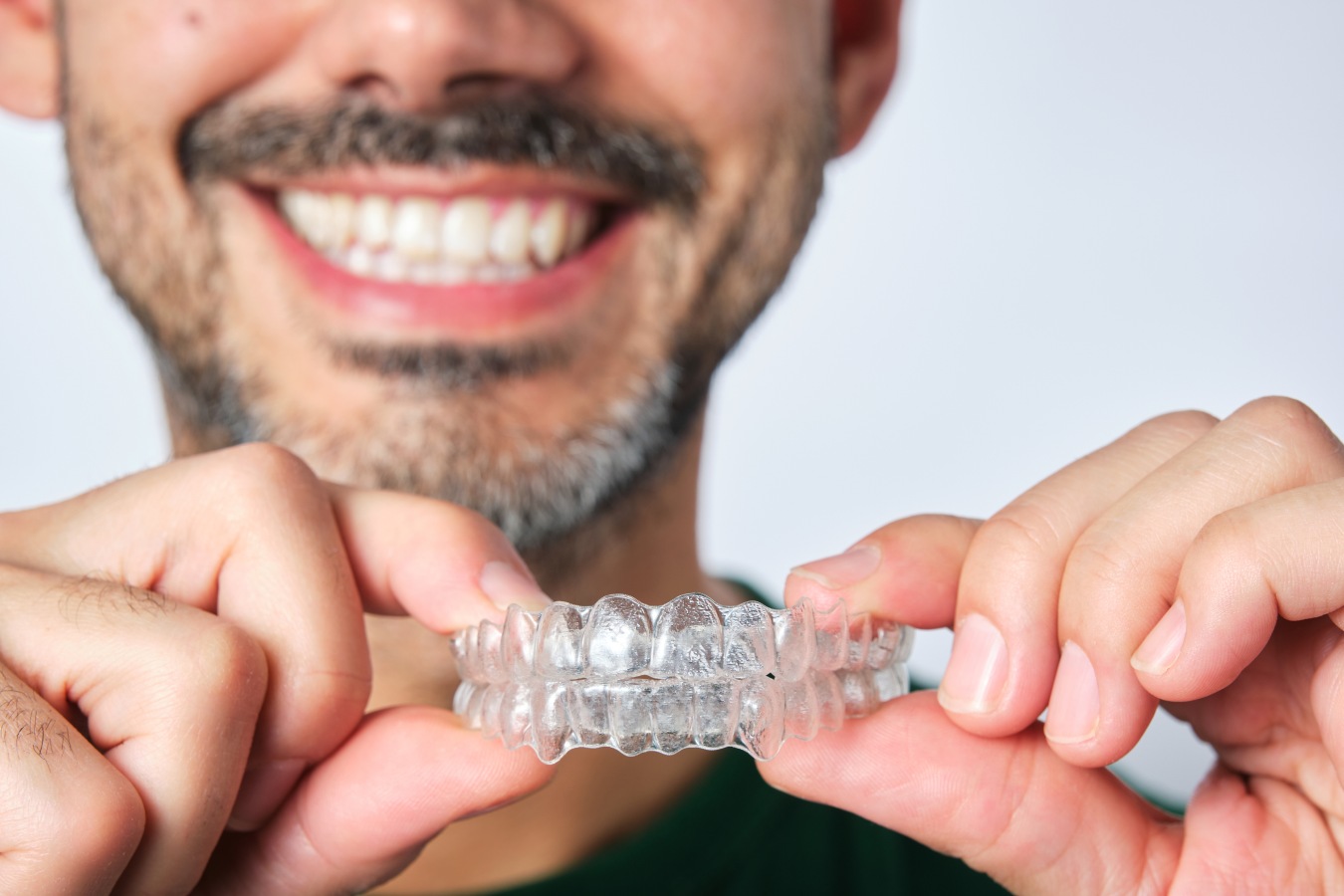 Smiling man holding a clear Invisalign aligner tray